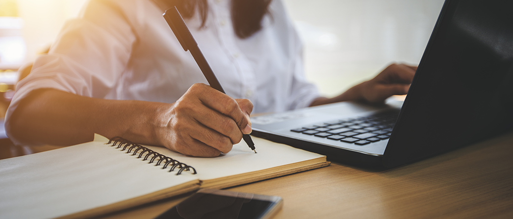 Person with a laptop making notes on a notepad