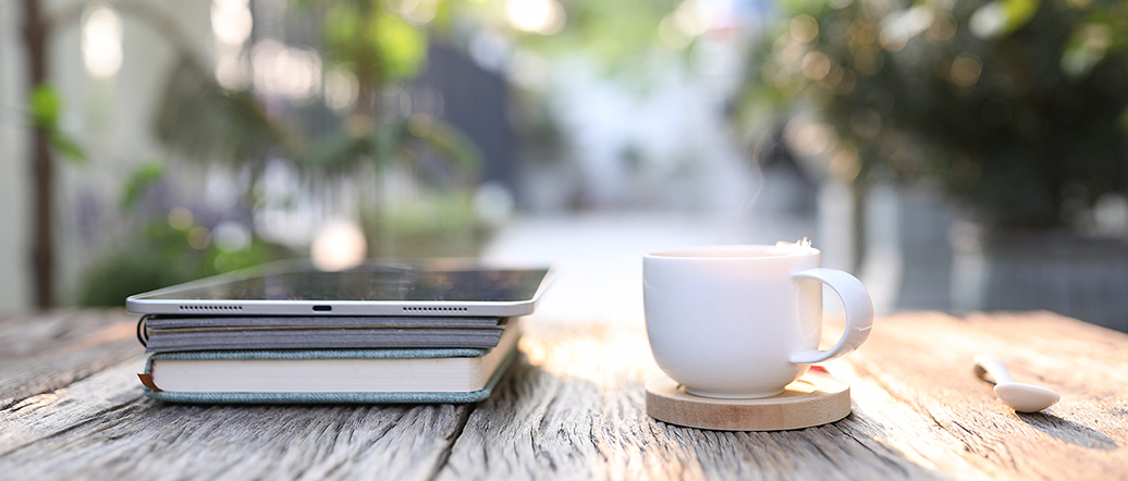 Books, tablet and coffee cup on a table outside in the summer