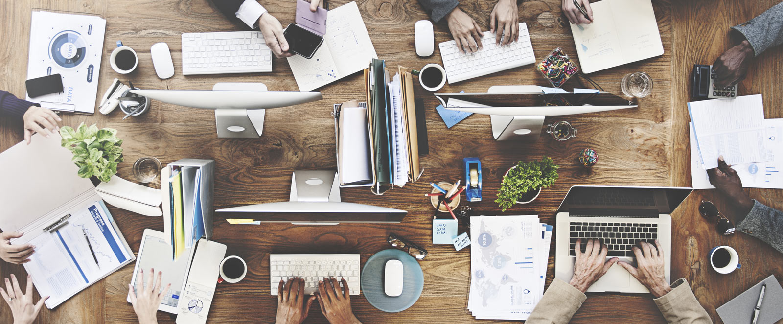 Desktop with books, laptops, people, papers, coffee, phones